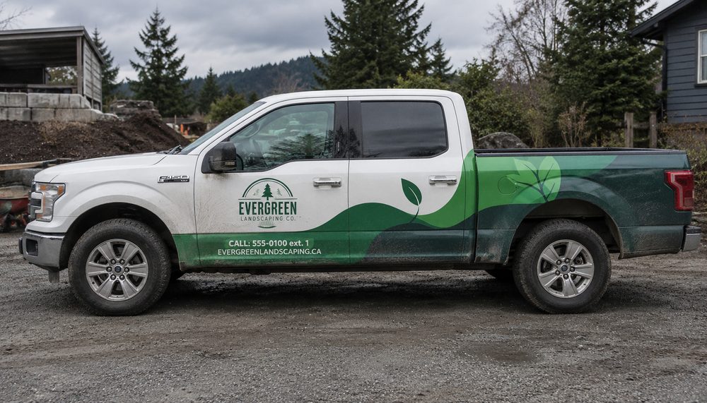 A crew-cab pickup in a green landscaping livery, leaf graphics sweeping from the doors across the bed