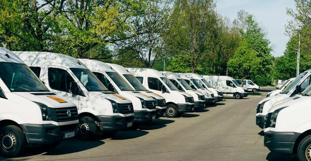A row of plain white panel vans parked nose-out, before any livery goes on