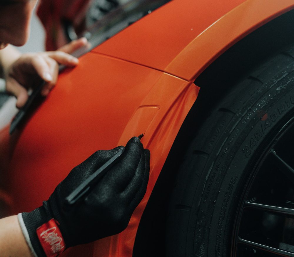 A fitter working film down along a wheel arch with a squeegee